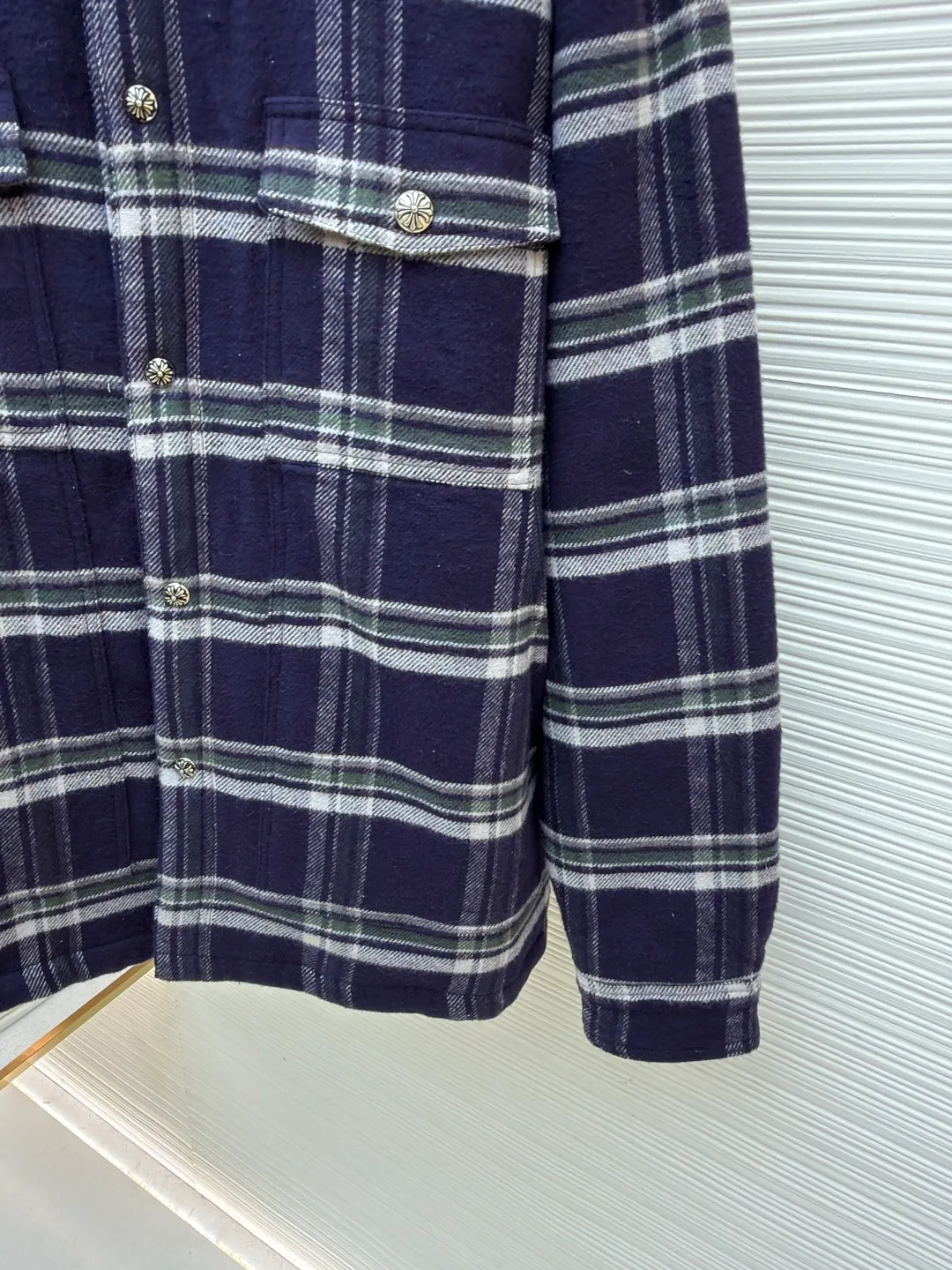 Chrome Hearts Contrast Checkered Lapel Shirt Jacket ●Item No.: 1682307-C05 ●Fabric: Cotton Fabric ●Technology: Made on Positioning Cutting Machine ●Color: Blue and White Plaid ●Version: Fitted ●Weight: Approximately 1030g ●Size: S-M-L-XL ●Description: This Louis Vuitton plaid shirt-style jacket is made of high-count wool blended brushed fabric imported from Italy. It is woven into a classic blue, white and green plaid pattern through yarn-dyed jacquard technology. The yarn is first dyed and then woven to ensure that the plaid color is clear and not easy to fade. The fabric has been pre-shrunk, and the shrinkage rate is controlled within 1%. The body pieces are cut using laser positioning, and the check pattern alignment error does not exceed 0.3cm. The double patch pockets on the front are sewn with welted three-dimensional sewing technology, and the edges of the pockets are padded for a crisper shape. The placket is equipped with custom metal engraved snap buttons, which accurately echo the plaid pattern of the body; the shoulders are made of seamless epaulette splicing technology, and the wiring is smooth and seamless. The double-needle locking technology on the cuffs and hem enhances durability. The overall stitch length is maintained at 7 needles per centimeter, and the wiring is even and smooth. The lining is made of breathable cotton and linen blended materials, taking into account texture and wearing comfort, fully demonstrating the brand's exquisite clothing technology. The overall wiring is straight and delicate, the fabric is comfortable and soft, and the color is consistent without color difference. It can be matched with the same style to create a fashionable look and control various occasions. Customized accessories, complete with three standards, same style for men and women!